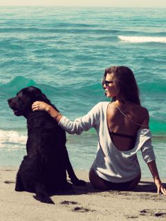 Девушка с черным псом на пляже