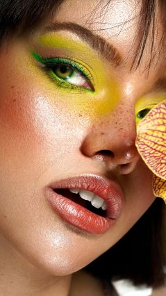 Женщина с зеленым и желтым макияжем, держащая цветок