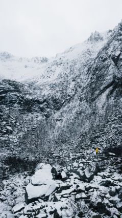 Крошечный человек в желтой куртке, стоящий между камнями, покрытыми снегом